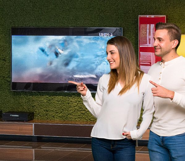 Eine Frau und ein Mann, die gemeinsam im HeimkinoWelt Showroom stehen und nach links zeigen.