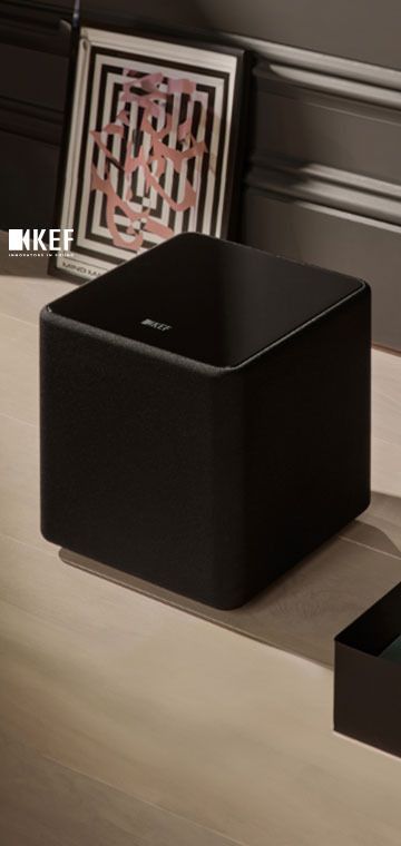 KEF Kube MIE Subwoofer auf dem Boden eines wohnlich eingerichteten Raums stehend.