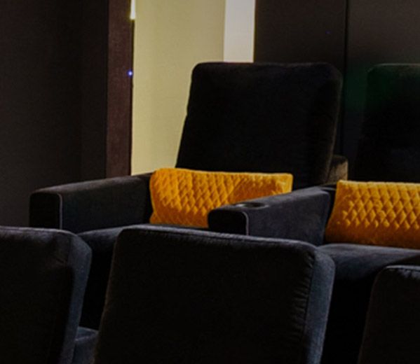 Foto von einem Heimkino, das von Roland Koller entworfen wurde. Zu sehen sind einige Sitzreihen mit orangenen Kissen, die zur Leinwand gerichtet sind.